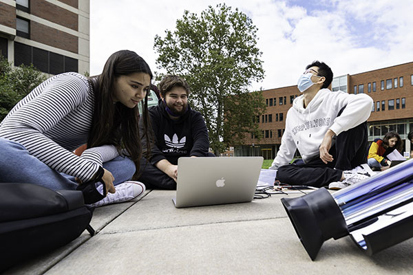 Three students gathered around a laptop computer in the Hajim quad.