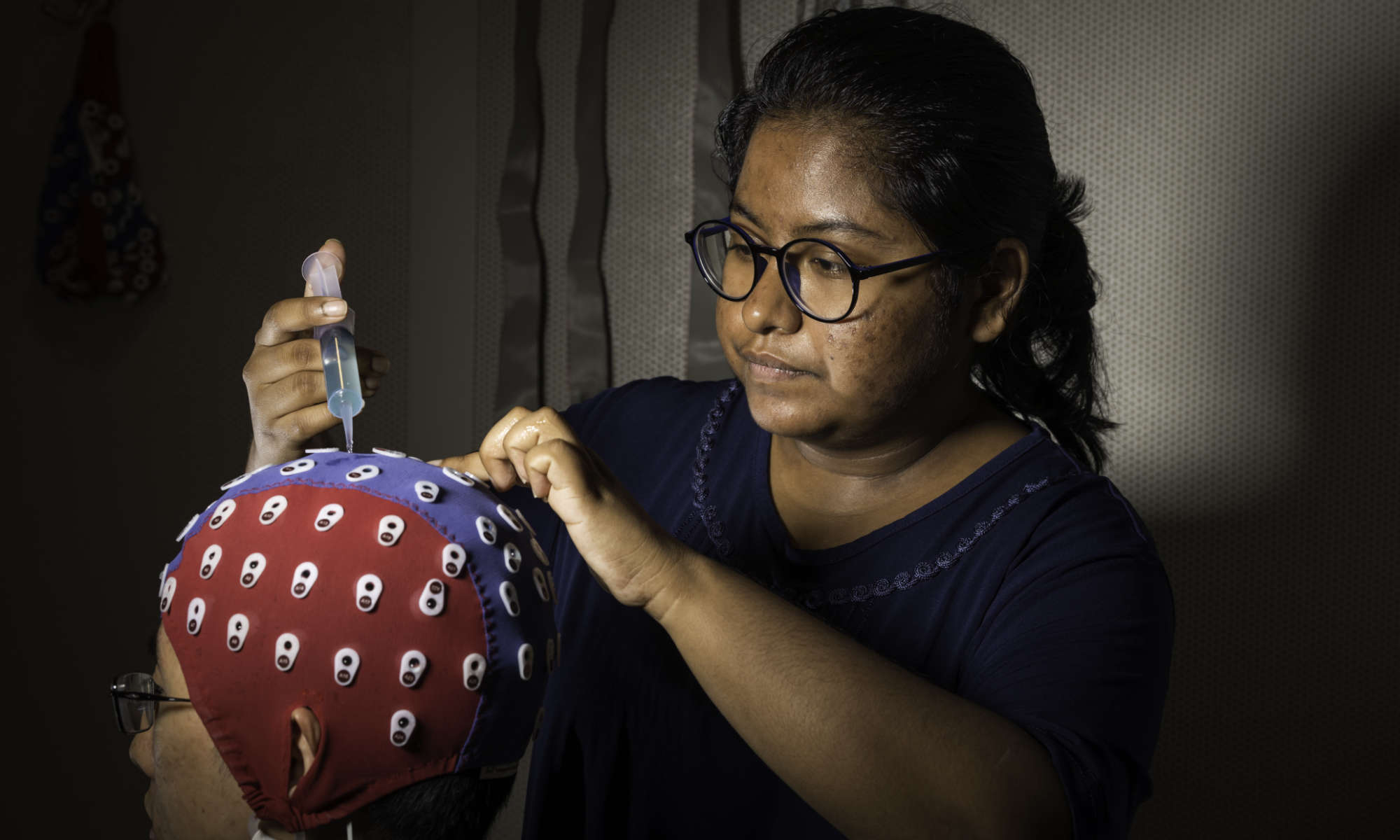 Biomedical engineering student adjusts an electroencephalography cap on a person.