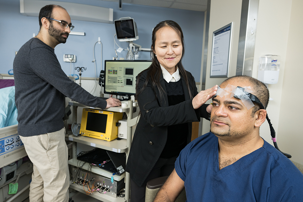 Researchers applying a sensor to a subject in an exam room.