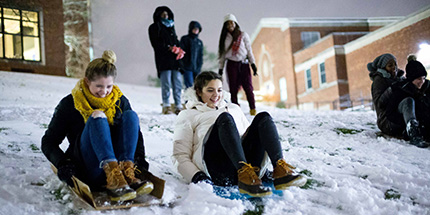 A group of students sledding at night in the winter snow.