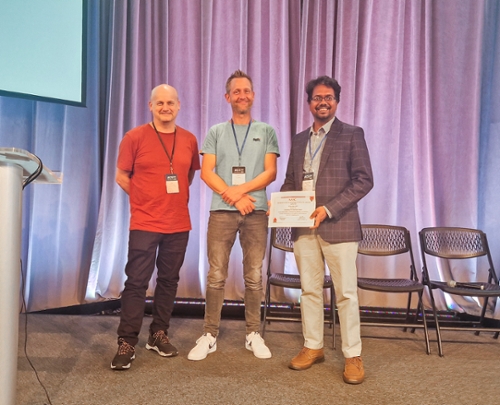 A group of three people standing and smiling at the camera with Raiyan Baten holding an award certificate.