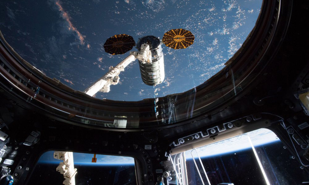 View from the International Space Station with a large white arm and tube in front of a blue space backdrop.