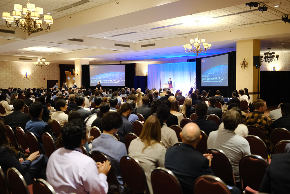 A view of a presentation as seen from behind attendees sitting in chairs.