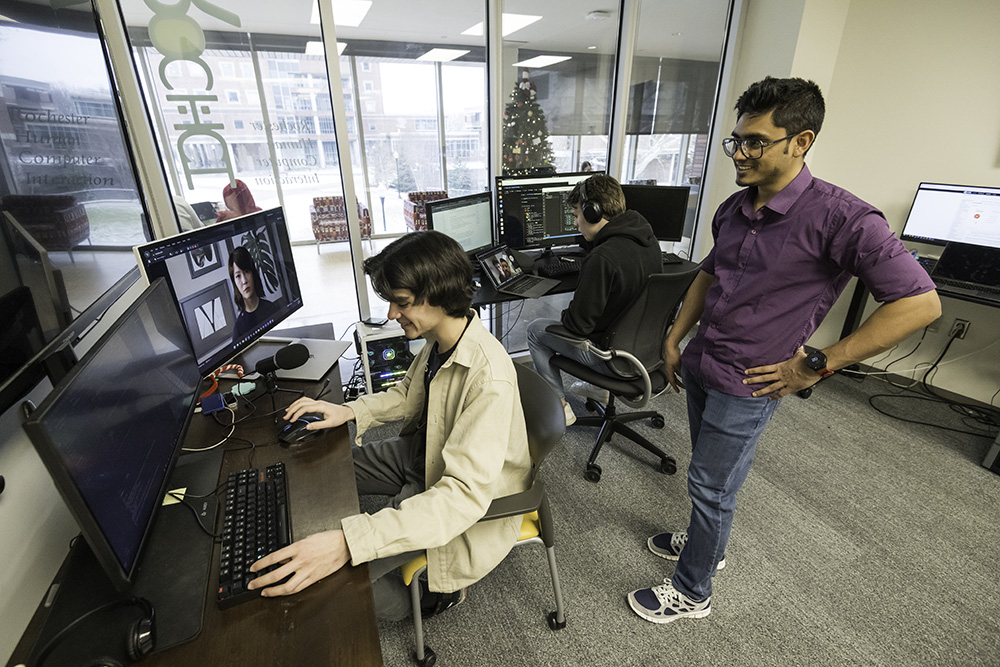 A student working at a computer while another person looks on.