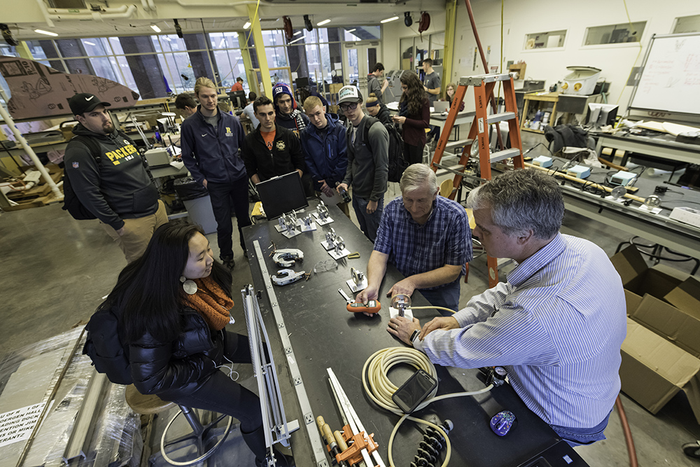 A professor using a tachometer to test air engines created by students.