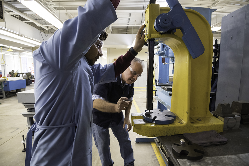 A professor supervises students as they work with an arbor press.