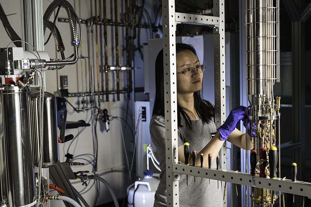 A student is pictured with a dilution refrigerator in a lab.