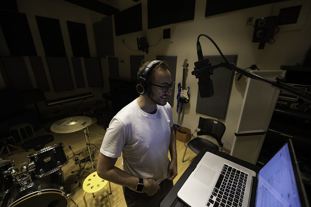 A student standing at a microphone recording sounds.