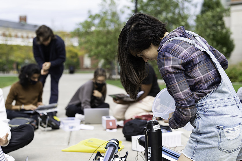 A student pouring liquid into a container during an experiment on the Hajim Quad.