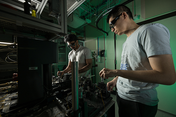 Two students working with equipment in a darkened lab space.