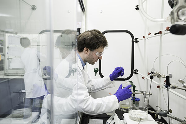 A student wearing a white coat working in a lab.