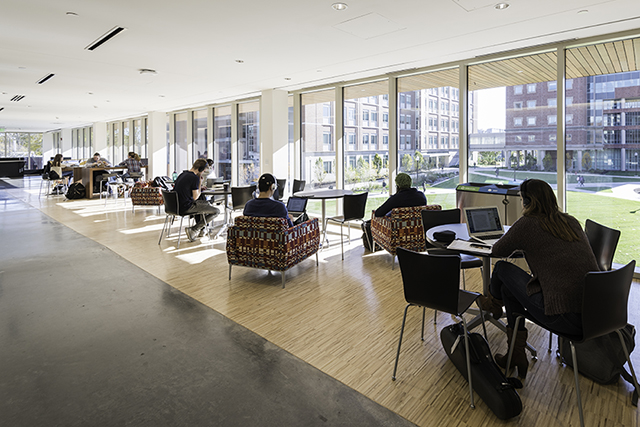 An interior view of students working in the lounge area of the 2nd floor of Wegmans Hall looking out over the Hajim Quad.