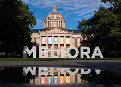 Exterior view of Rush Rhees library with large Meliora letters in foreground.