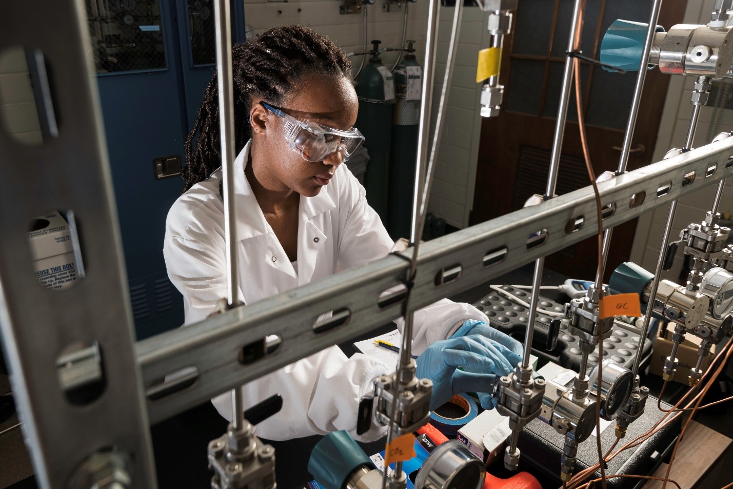 A student wearing a lab coat and goggles works in a lab.