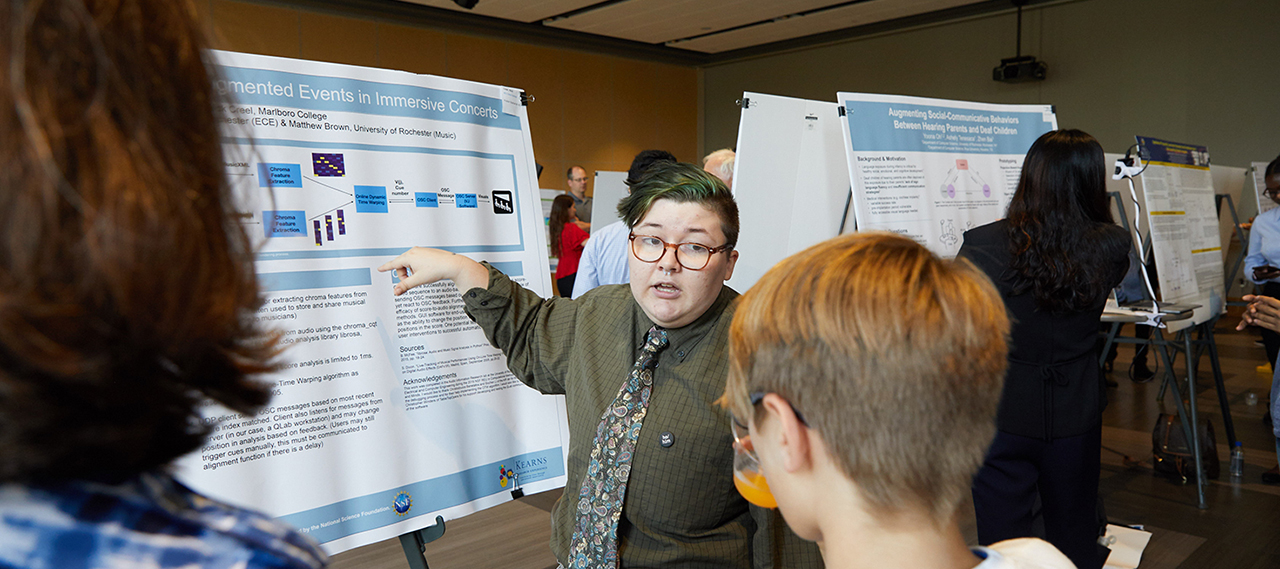 A student describing their research at a poster session.