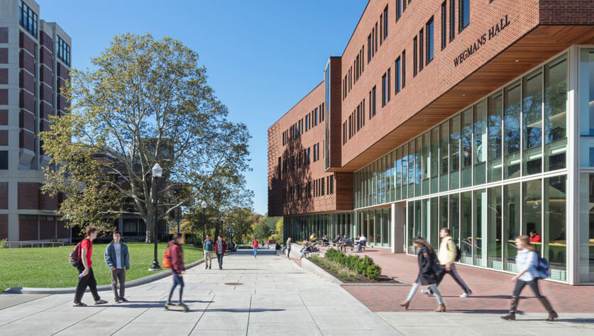 An exterior view of the front of Wegmans Hall with students walking by.