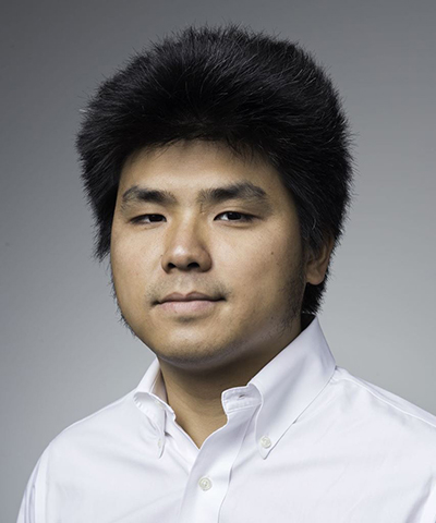 man in a light blue shirt looking at the camera against a gray background