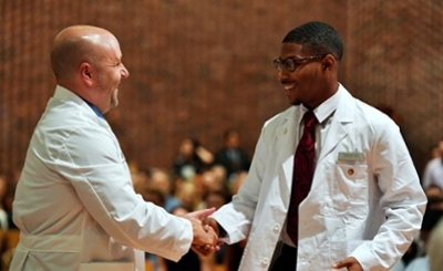 A graduate and doctor shaking hands at the white coat ceremony.