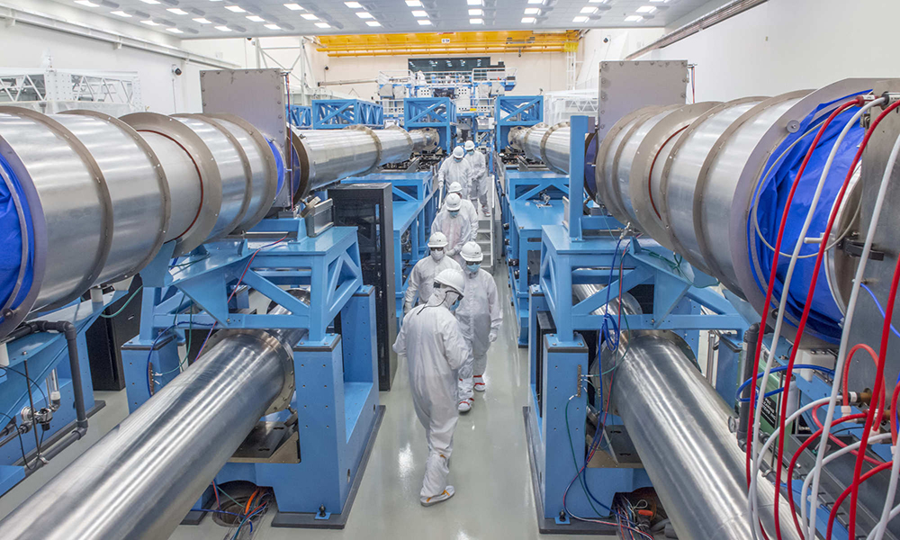 Workers in white protective gear walk through a laser facility.