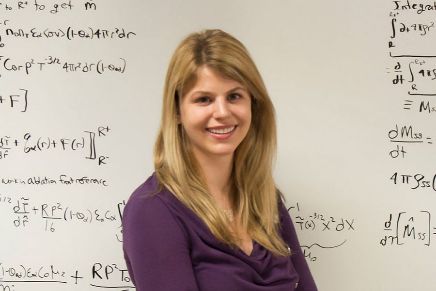 Alison Christopherson facing the camera in front of a whiteboard with equations on it.
