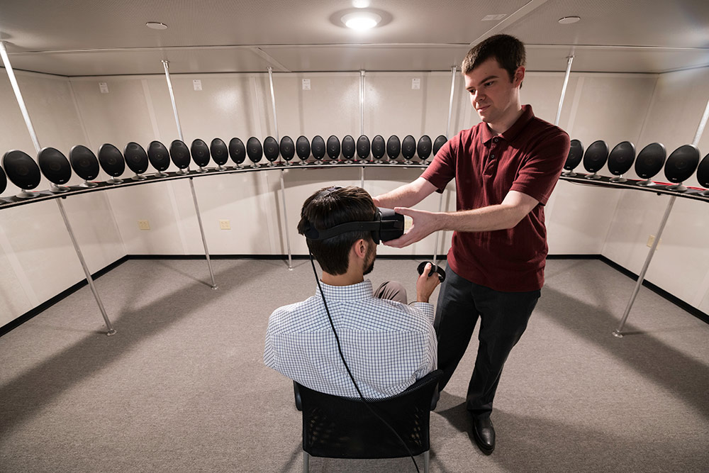 Biomedical engineering graduate student Tom Stoll, right, adjusts a virtual reality head-mounted display on assistant professor Ross Maddox.