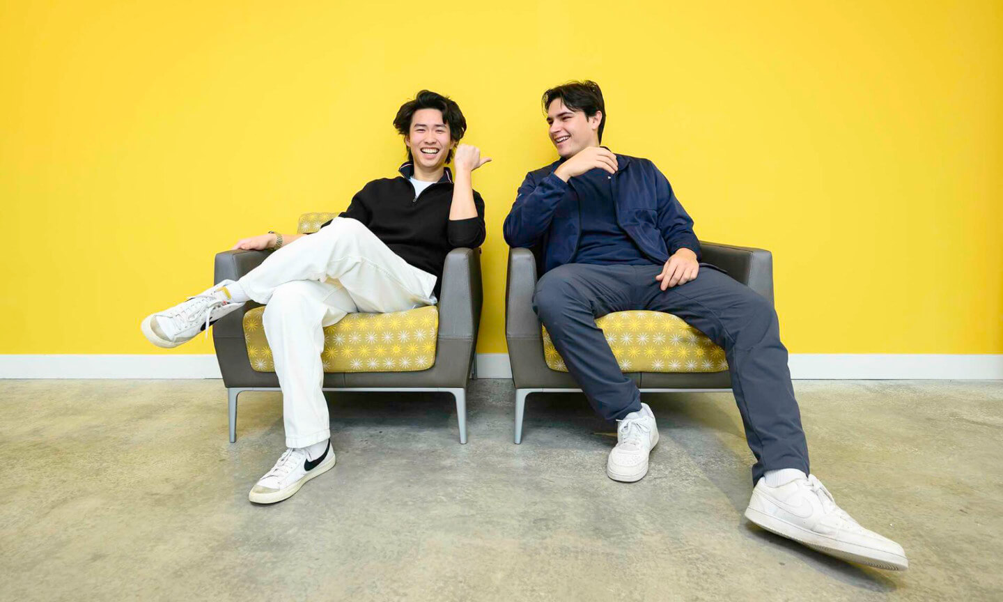Steve Lim and Walter McDonald smile while seated in chairs against a bright yellow background